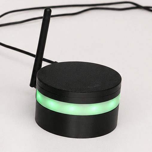 The Medication Diary base station: a small black puck with an antenna and a glowing green light ring.